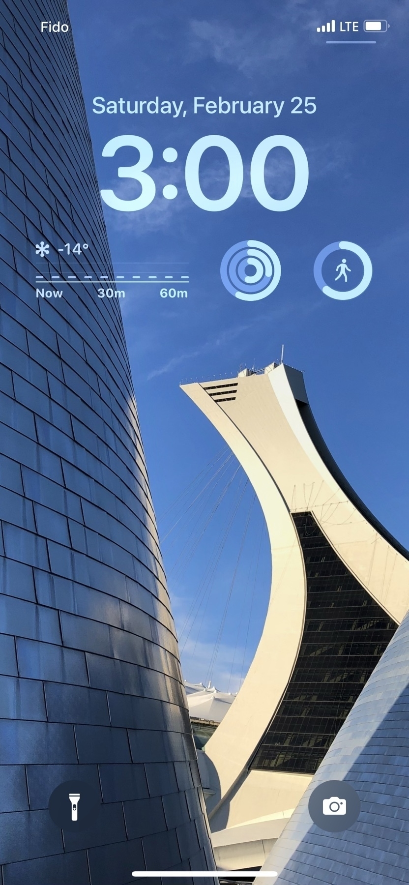 A screenshot of an iPhone lock screen showing the Montreal Tower at the Olympic Park between the twin domes of the Montreal Planetarium.